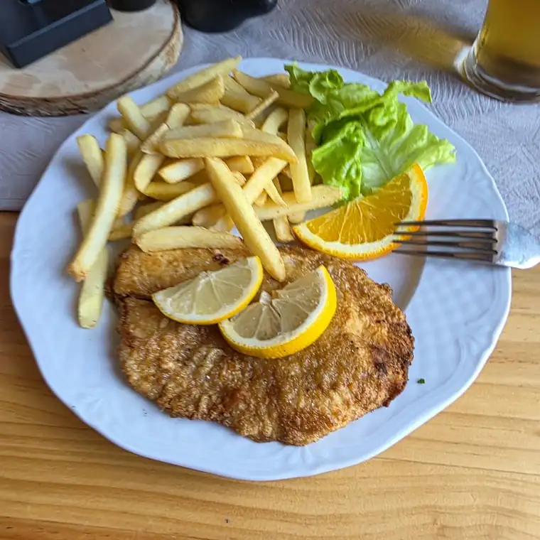 Panierowany kotlet z frytkami i cytryną na białym talerzu