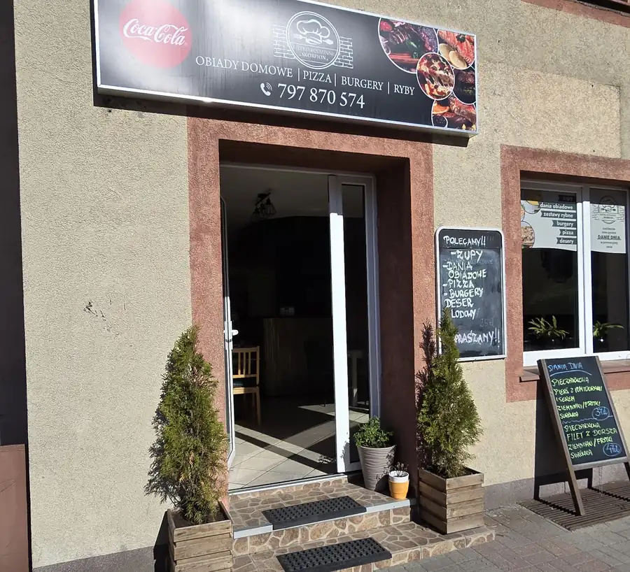 Wejście do bistro z czarnym szyldem, roślinami w donicach i tablicą